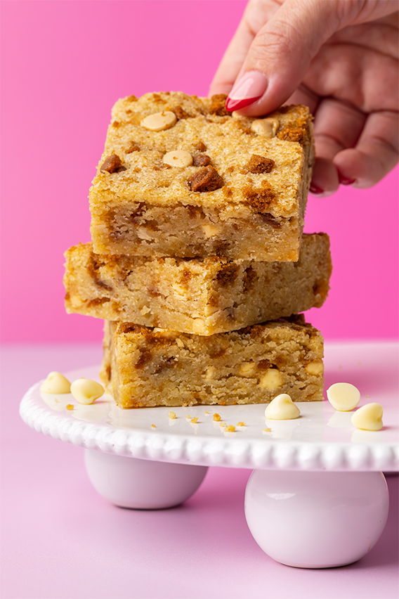 Caramel Biscuit Blondie Stacked on plate with hand grabbing top blondie