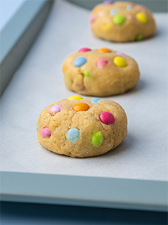 Gingerbread cookie dough balls with rainbow chocolate beans on baking tray